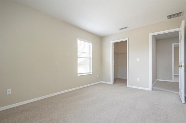 unfurnished bedroom with light carpet, a walk in closet, and a closet