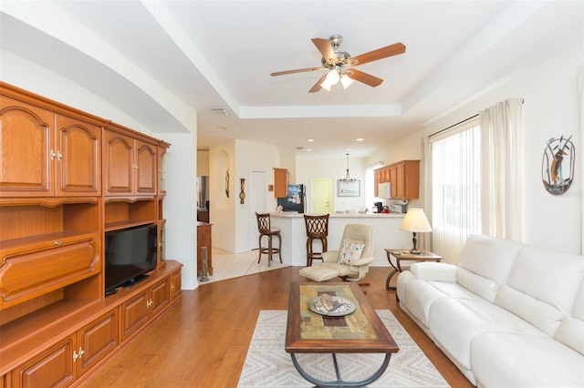 living room featuring a raised ceiling, ceiling fan, and light hardwood / wood-style flooring