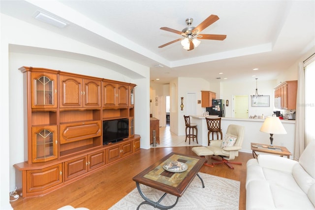 living room with a raised ceiling, light hardwood / wood-style floors, and ceiling fan