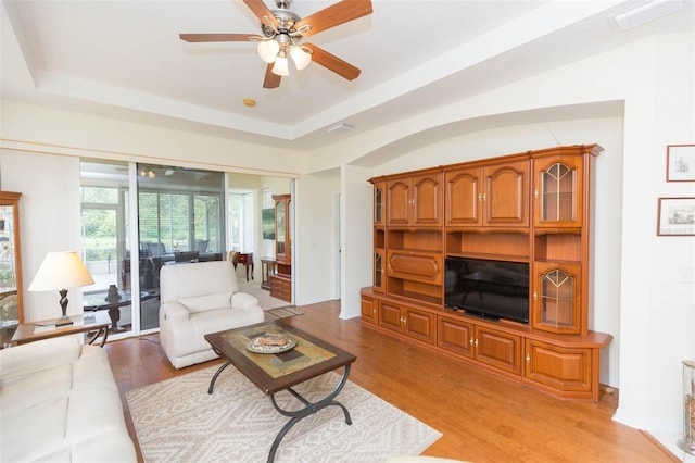 living room with ceiling fan, a raised ceiling, and light hardwood / wood-style floors