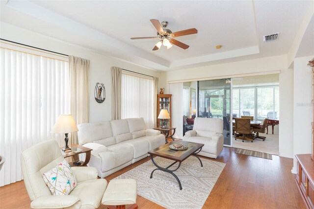 living room featuring wood-type flooring, a tray ceiling, and ceiling fan