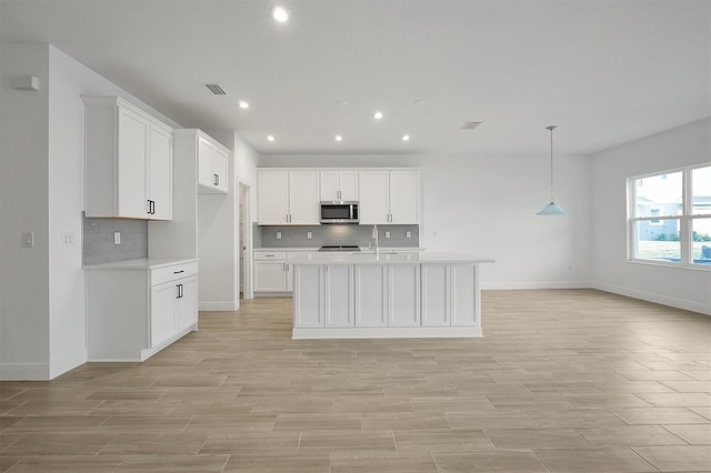 kitchen with sink, hanging light fixtures, an island with sink, tasteful backsplash, and white cabinetry