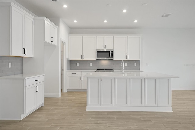 kitchen featuring a center island with sink, stove, white cabinetry, and sink