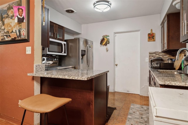 kitchen with appliances with stainless steel finishes, tasteful backsplash, a breakfast bar, sink, and dark brown cabinetry