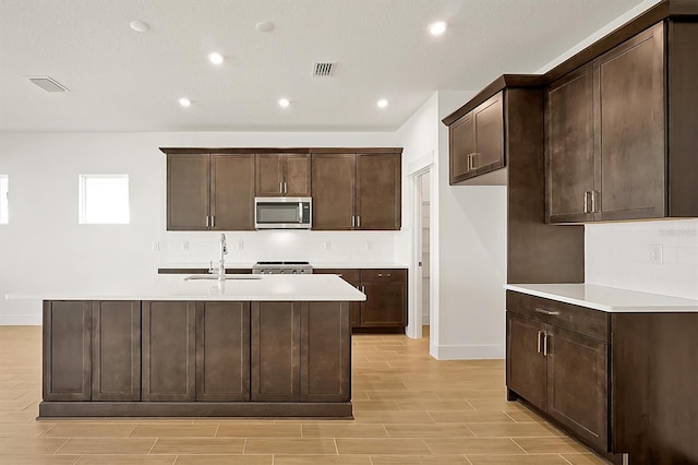 kitchen featuring dark brown cabinets, an island with sink, range, and sink