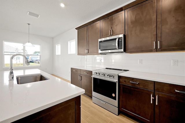 kitchen with sink, hanging light fixtures, decorative backsplash, dark brown cabinets, and appliances with stainless steel finishes