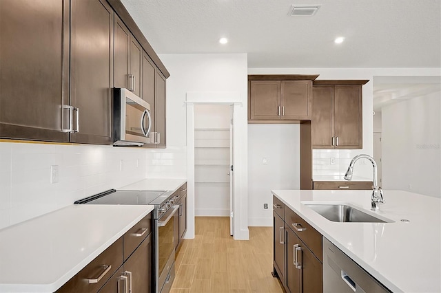 kitchen with tasteful backsplash, sink, light hardwood / wood-style flooring, and appliances with stainless steel finishes