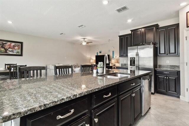 kitchen with stone counters, sink, ceiling fan, a kitchen bar, and a center island with sink