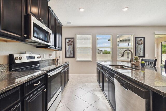 kitchen with stainless steel appliances, sink, dark stone counters, light tile patterned flooring, and a textured ceiling