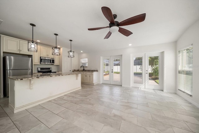 kitchen with ceiling fan, a center island, stainless steel appliances, light stone counters, and cream cabinets