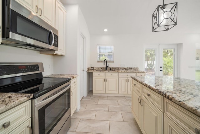 kitchen with hanging light fixtures, cream cabinetry, light stone counters, and stainless steel appliances