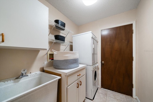 clothes washing area featuring light tile patterned floors, stacked washer / dryer, a textured ceiling, cabinets, and sink