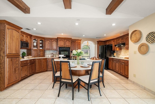 kitchen with beam ceiling, decorative backsplash, black appliances, and a center island with sink