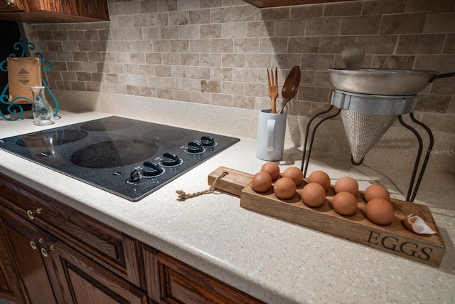 interior details featuring black electric stovetop, backsplash, and dark brown cabinetry