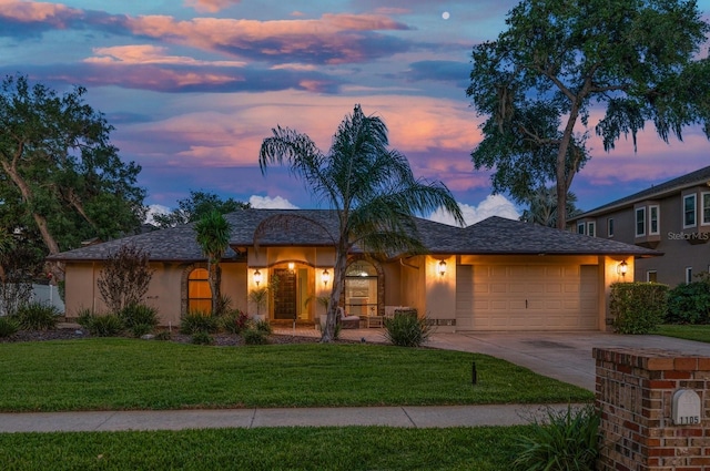 view of front of house with stucco siding, an attached garage, driveway, and a yard