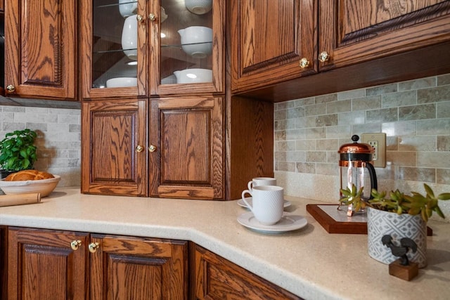 kitchen with brown cabinetry, light countertops, glass insert cabinets, and tasteful backsplash