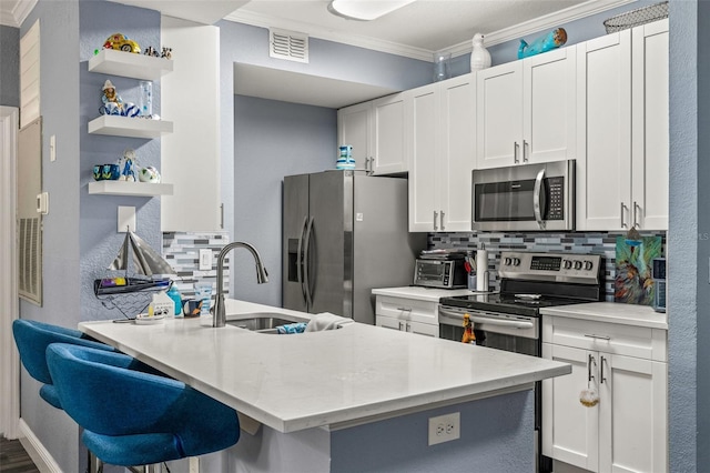 kitchen featuring sink, white cabinets, a kitchen bar, tasteful backsplash, and appliances with stainless steel finishes