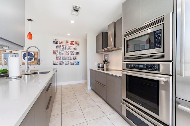 kitchen featuring gray cabinetry, light tile patterned floors, hanging light fixtures, stainless steel appliances, and wall chimney exhaust hood