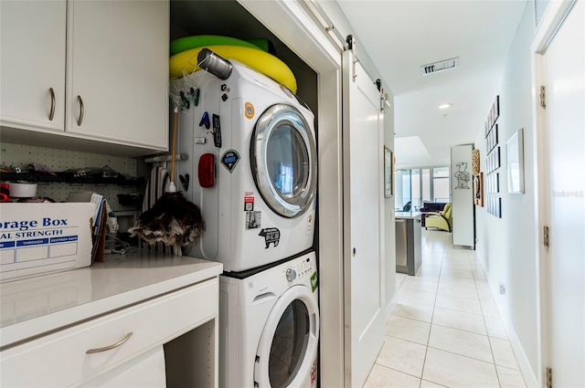 laundry room featuring stacked washer and clothes dryer, a barn door, and light tile patterned flooring