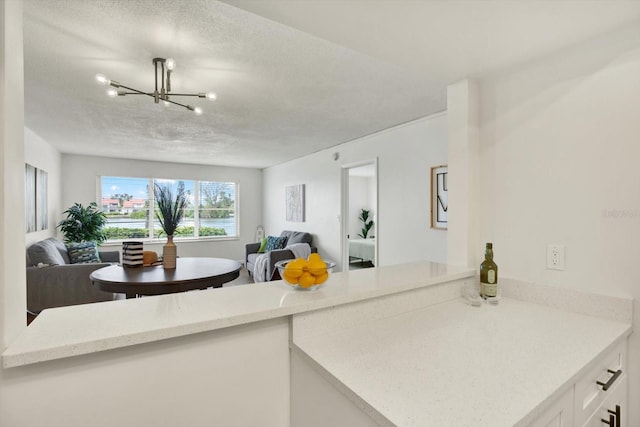 kitchen with white cabinetry, kitchen peninsula, light stone countertops, a textured ceiling, and a notable chandelier