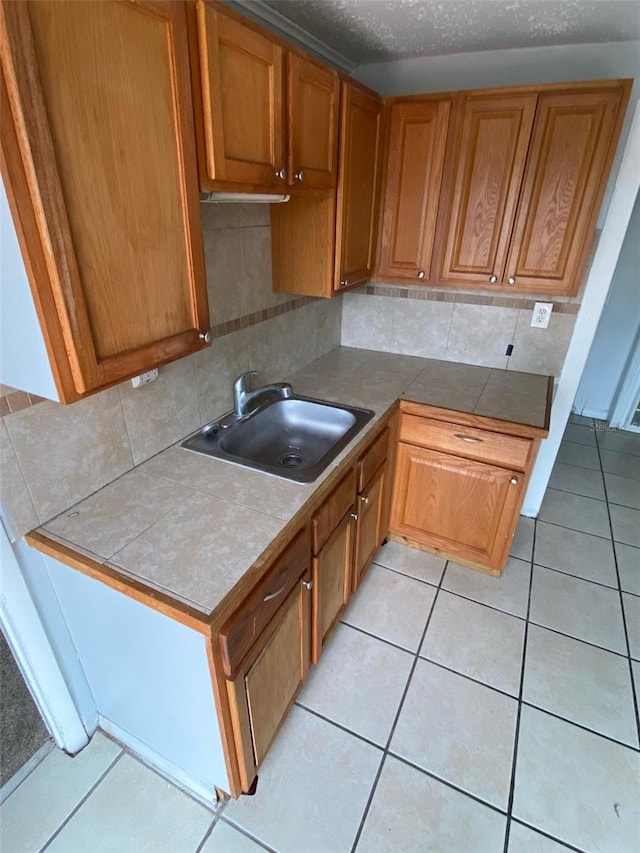 kitchen with light tile patterned floors, a textured ceiling, backsplash, and sink