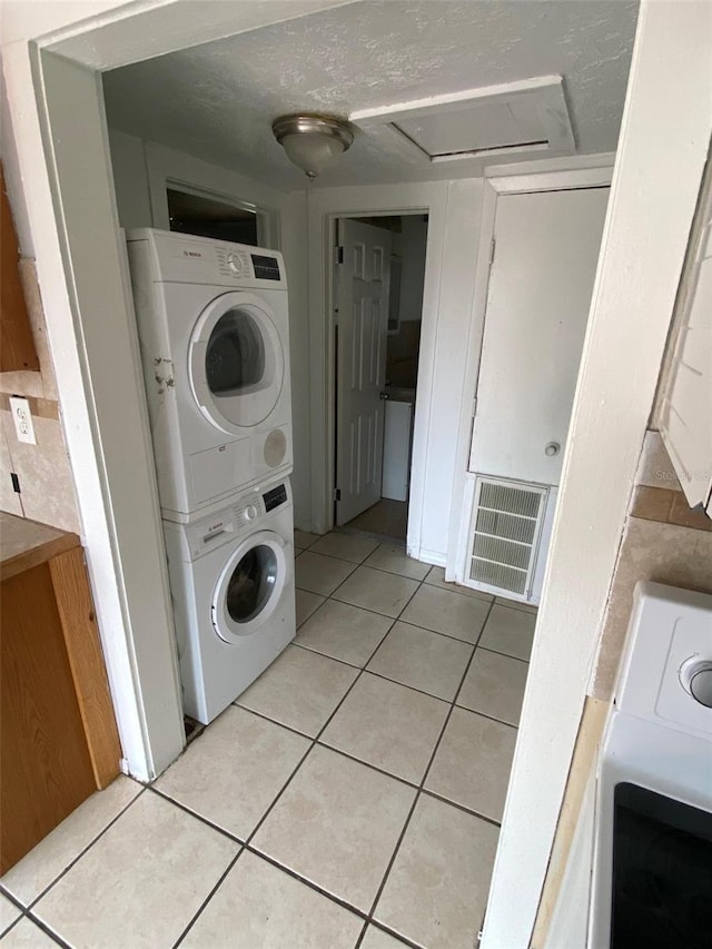 clothes washing area featuring light tile patterned floors and stacked washer and clothes dryer