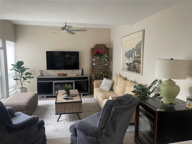 living room with a textured ceiling, ceiling fan, and light wood-type flooring