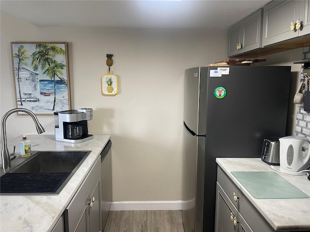 kitchen with gray cabinets, appliances with stainless steel finishes, wood-type flooring, and sink