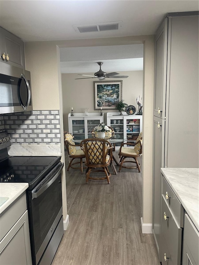 kitchen with gray cabinetry, backsplash, stainless steel appliances, ceiling fan, and light wood-type flooring