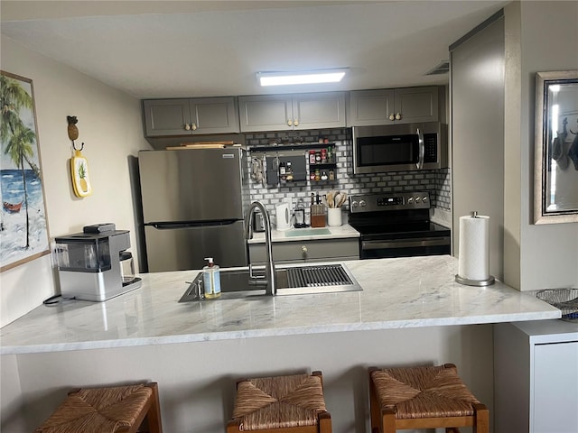 kitchen featuring a breakfast bar, stainless steel appliances, gray cabinetry, and kitchen peninsula