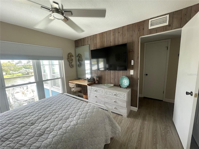 bedroom featuring ceiling fan, wooden walls, wood-type flooring, and a textured ceiling