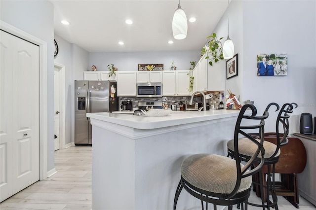 kitchen with pendant lighting, appliances with stainless steel finishes, tasteful backsplash, kitchen peninsula, and white cabinets