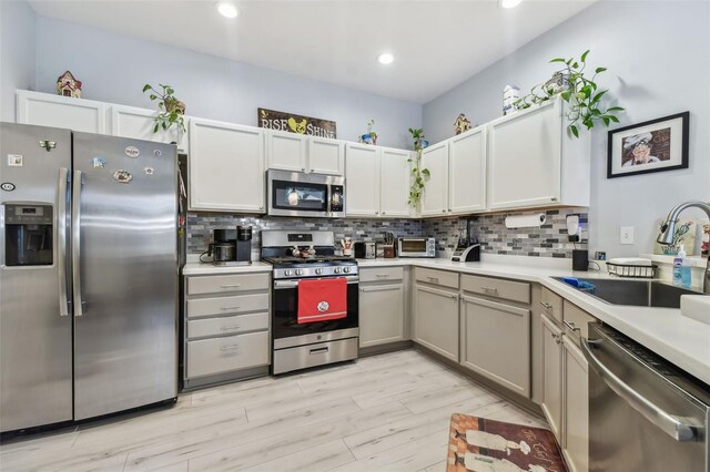 kitchen with backsplash, stainless steel appliances, sink, and light hardwood / wood-style floors