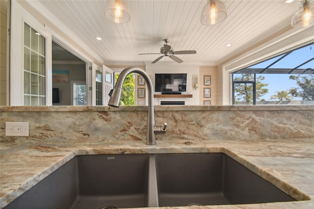 interior details featuring wood ceiling, light stone counters, a fireplace, ceiling fan, and sink