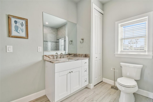 bathroom with wood-type flooring, toilet, vanity, and tiled shower