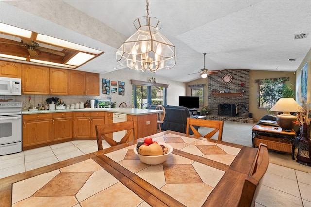 dining space with ceiling fan with notable chandelier, a fireplace, vaulted ceiling, and light tile patterned flooring