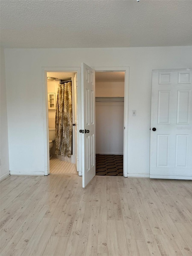 unfurnished bedroom with a textured ceiling, a closet, light hardwood / wood-style floors, and ensuite bath