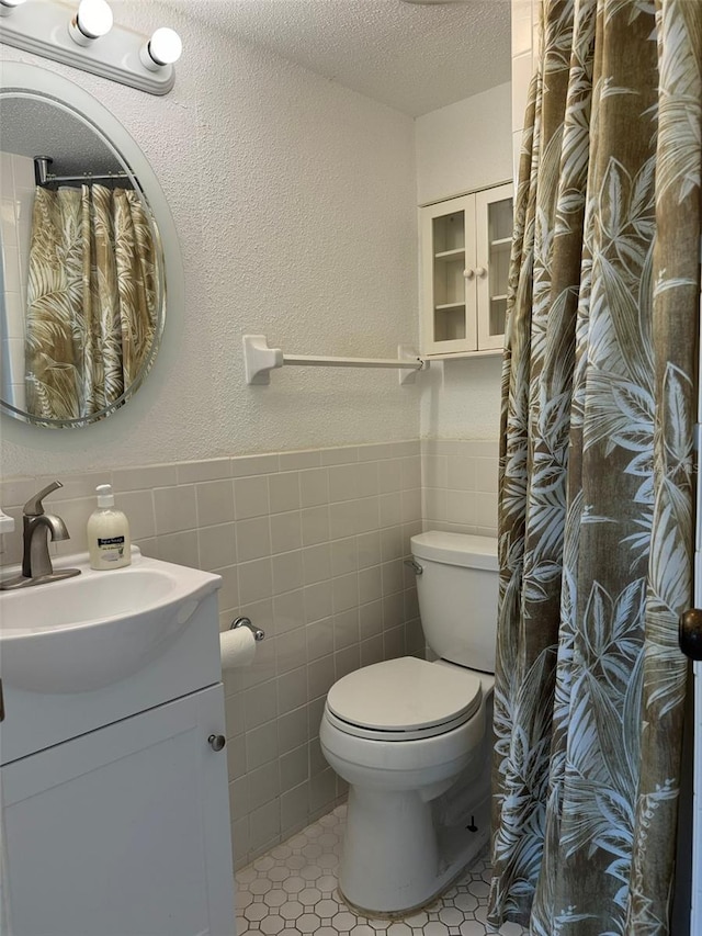 bathroom featuring a textured ceiling, tile patterned flooring, vanity, tile walls, and toilet