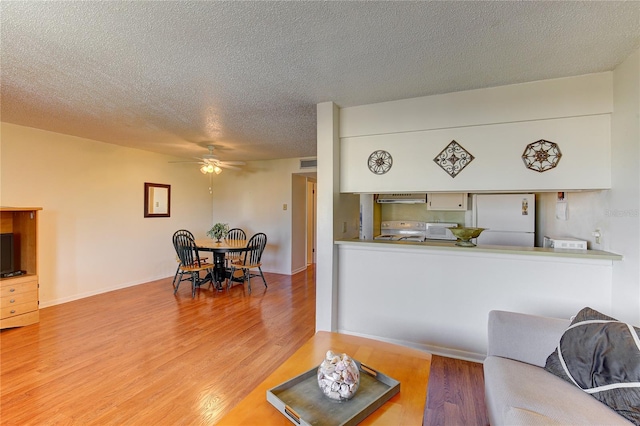 living room featuring ceiling fan, a textured ceiling, and light wood-type flooring