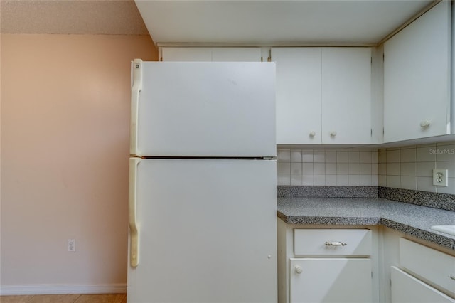 kitchen with white refrigerator, white cabinetry, and backsplash