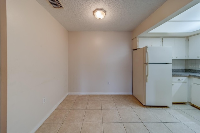 kitchen featuring white cabinetry, a textured ceiling, decorative backsplash, white refrigerator, and light tile patterned flooring