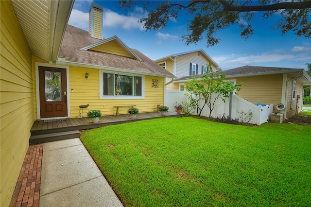 exterior space featuring a chimney, roof with shingles, fence, a deck, and a yard