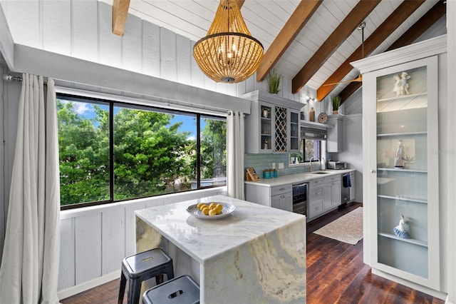 kitchen featuring dark wood-type flooring, sink, light stone countertops, decorative light fixtures, and beam ceiling