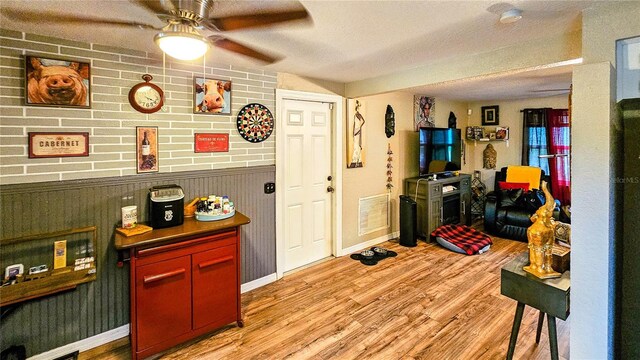 interior space featuring wooden walls, a textured ceiling, light wood-type flooring, and ceiling fan