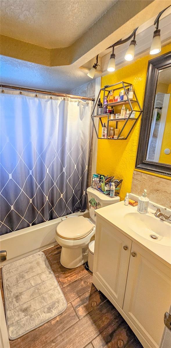 full bathroom with hardwood / wood-style flooring, toilet, shower / bath combination with curtain, vanity, and a textured ceiling