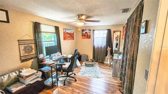 home office with a wealth of natural light, a textured ceiling, wood-type flooring, and ceiling fan