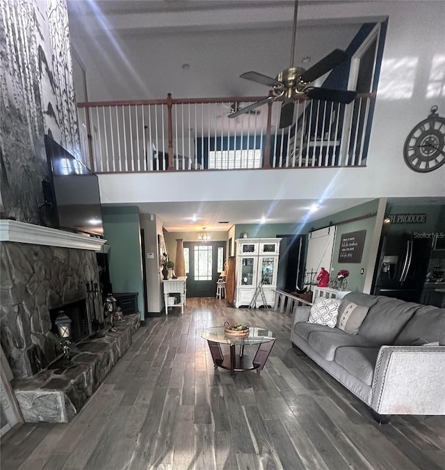 living room featuring a towering ceiling, hardwood / wood-style flooring, ceiling fan, and a stone fireplace