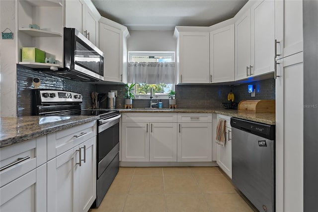 kitchen with white cabinets, light tile patterned floors, appliances with stainless steel finishes, light stone counters, and decorative backsplash