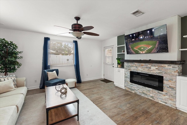 living room featuring ceiling fan, a stone fireplace, and wood-type flooring