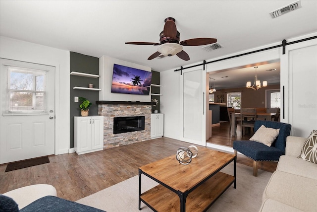 living room featuring hardwood / wood-style floors, ceiling fan with notable chandelier, built in shelves, a barn door, and a fireplace